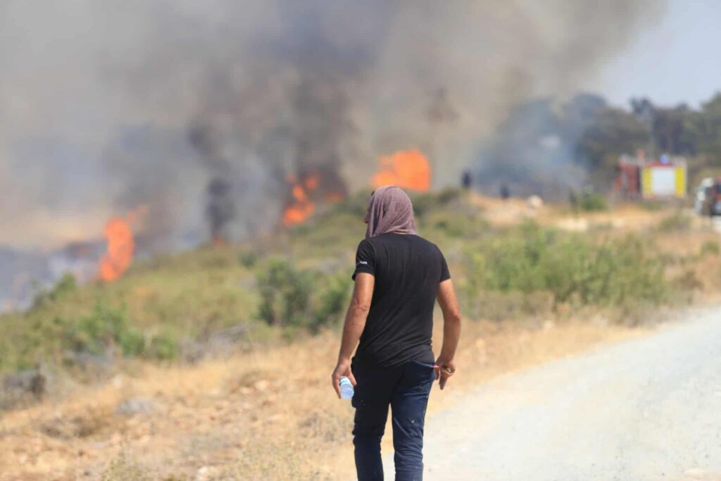 εικόνα που δείχνει κάτοικο με πετσέτα στο κεφάλι κοιτάζει από απόσταση τις φλόγες που κατακαίνε δάση και περιουσίες
