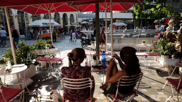εικόνα που δείχνει δύο γυναίκες να κάθονται σε καφέ στο Μοναστηράκι ενώ στο φόντο φαίνεται γεμάτη η πλατεία