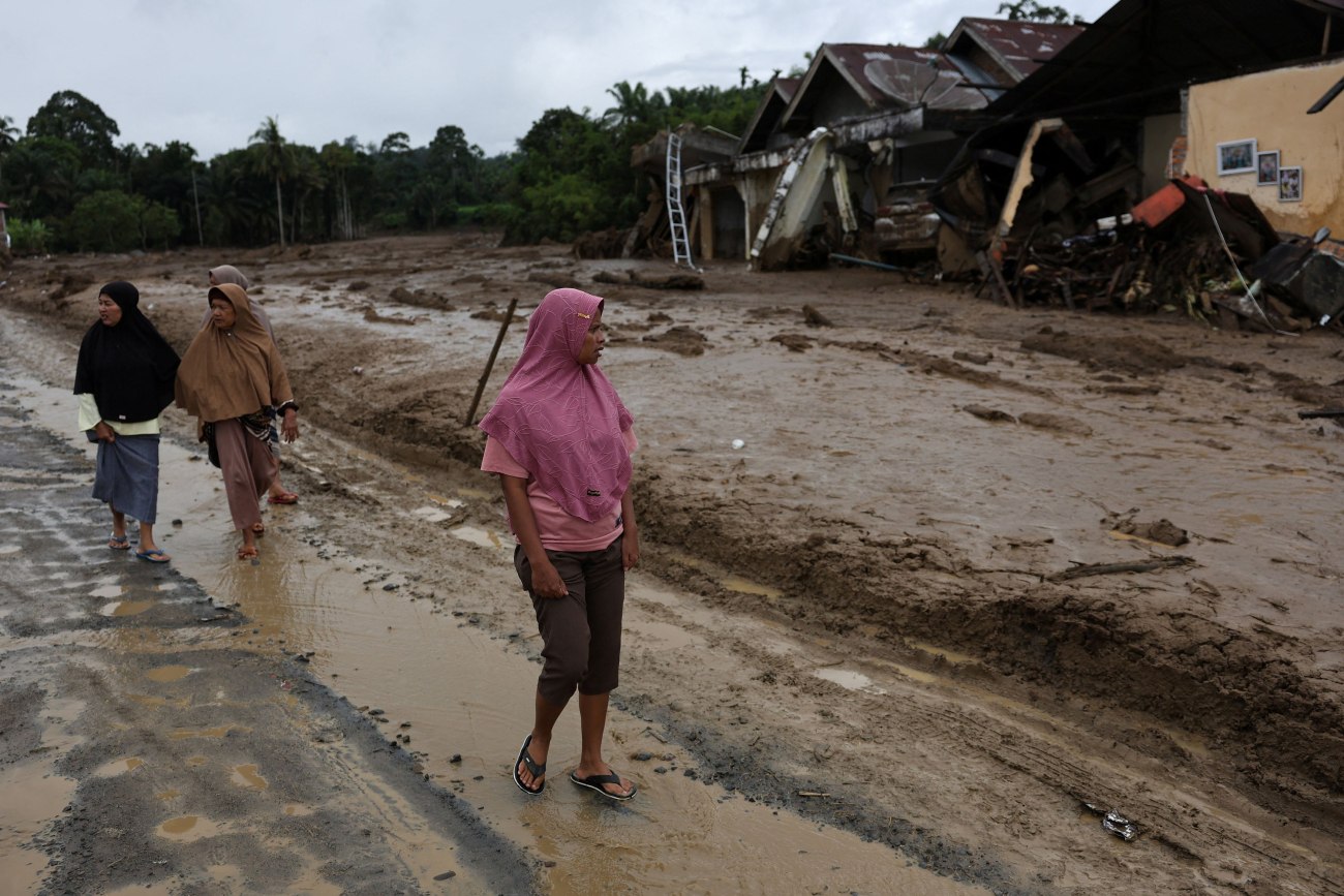 εικόνα που δείχνουν γυναίκες στην Ινδονησία να περπατούν στα λασπόνερα κοιτάζοντας γύρω τους την τεράστια καταστροφή 