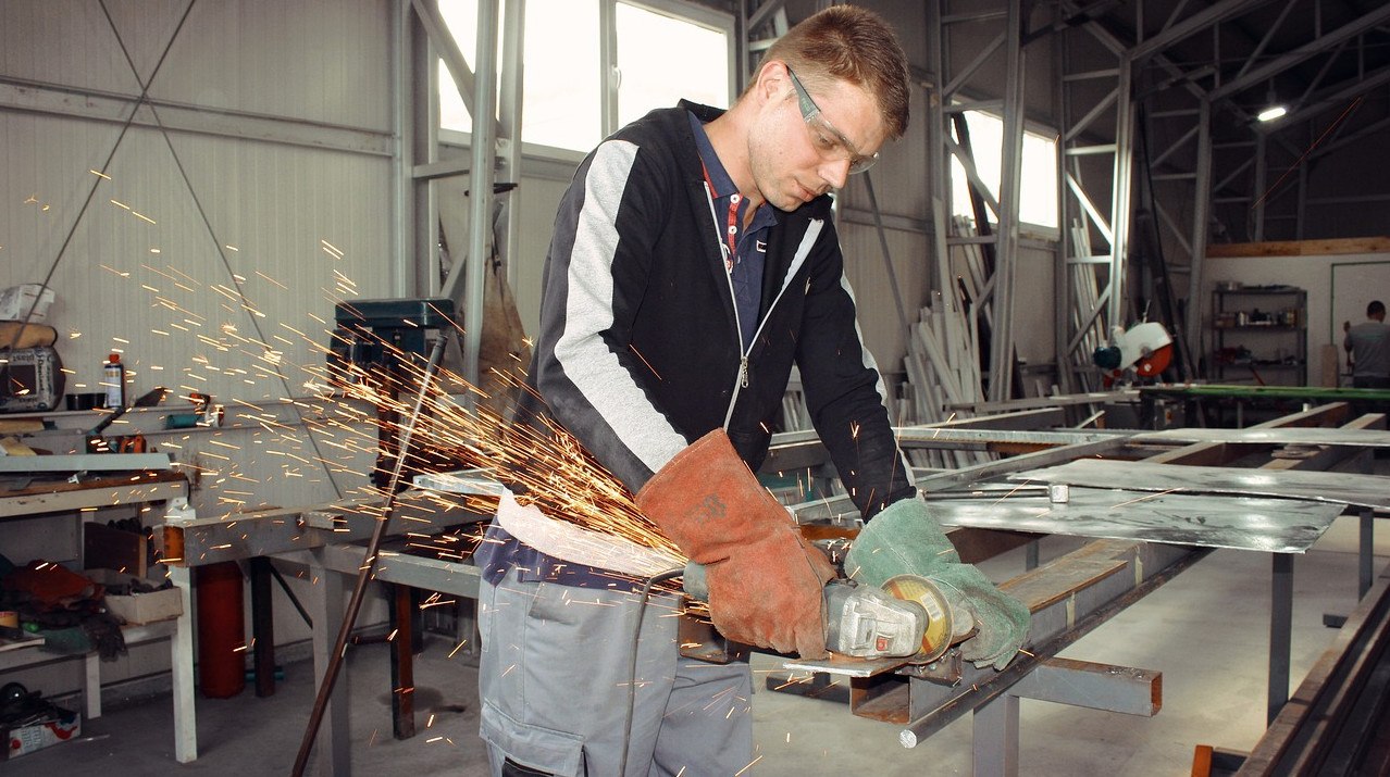 εικόνα που δείχνει εργάτη σε βιομηχανική μονάδα να κόβει μέταλλο με τον τροχό