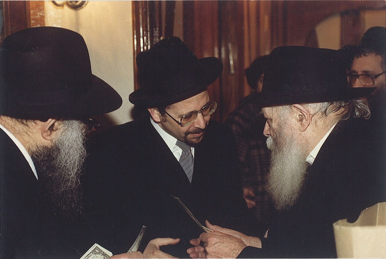 Ο Αχαρόν Ντάουμ (στο κέντρο) συνομιλεί με τον Ρέμπε (δεξιά) κατά τη διάρκεια της διανομής δολαρίων για φιλανθρωπικούς σκοπούς