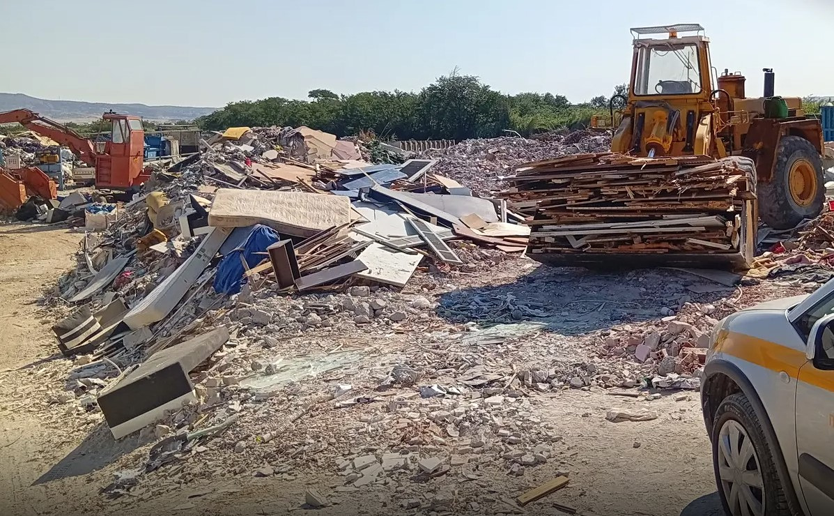 εικόνα που δείχνει γερανοφόρο όχημα και φορτωτή για ξύλα ανάμεσα σε σωρούς αποβλήτων